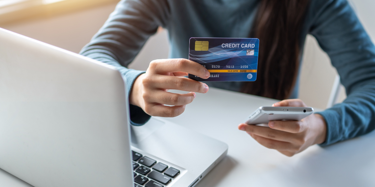 Hand håller bankkort framför datorskärm, symbol för bankbedrägeri efter bluffsamtal från falsk bankman.