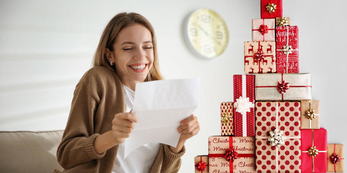 En kvinna är glad över ett prev och en stapel med julklappar. SPP har ett ovanligt förslag till årets julklapp i år och föreslår att arbetsgivare ska stoppa tjänstepensionen i paketet i stället för andra julgåvor till sina anställda.