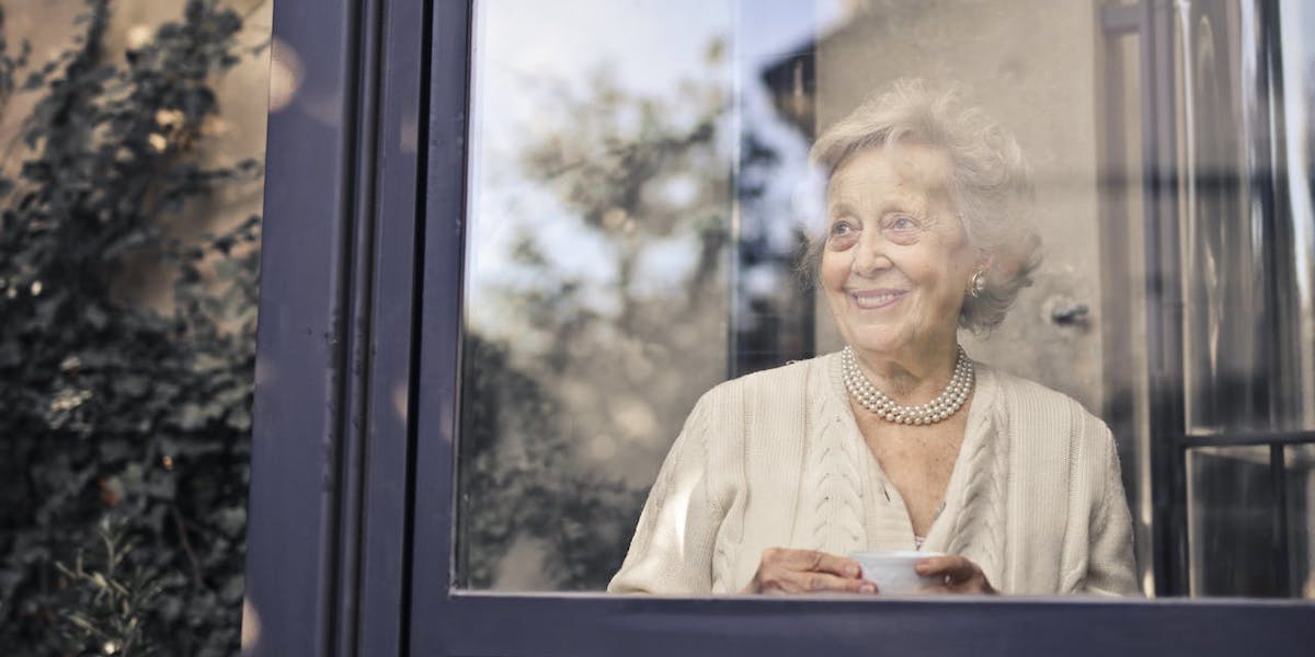 en kvinna tittar ut genom ett stort fönster. Hon har byggt upp ett ekonomiskt skyddsnät genom att sparat småsummor i nästan 40 år och det gör bland annat att hon kan bo kvar i sitt stora fina hus. Kvinnan på bilden har ingenting med texten att göra.