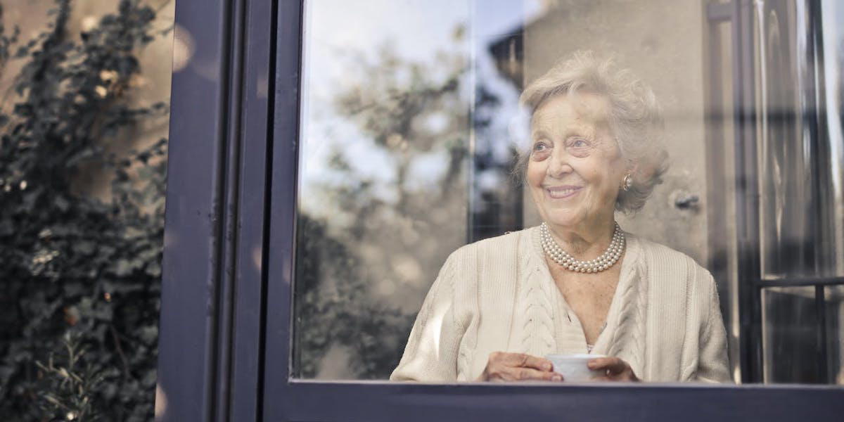 en kvinna tittar ut genom ett stort fönster. Hon har byggt upp ett ekonomiskt skyddsnät genom att sparat småsummor i nästan 40 år och det gör bland annat att hon kan bo kvar i sitt stora fina hus. Kvinnan på bilden har ingenting med texten att göra.