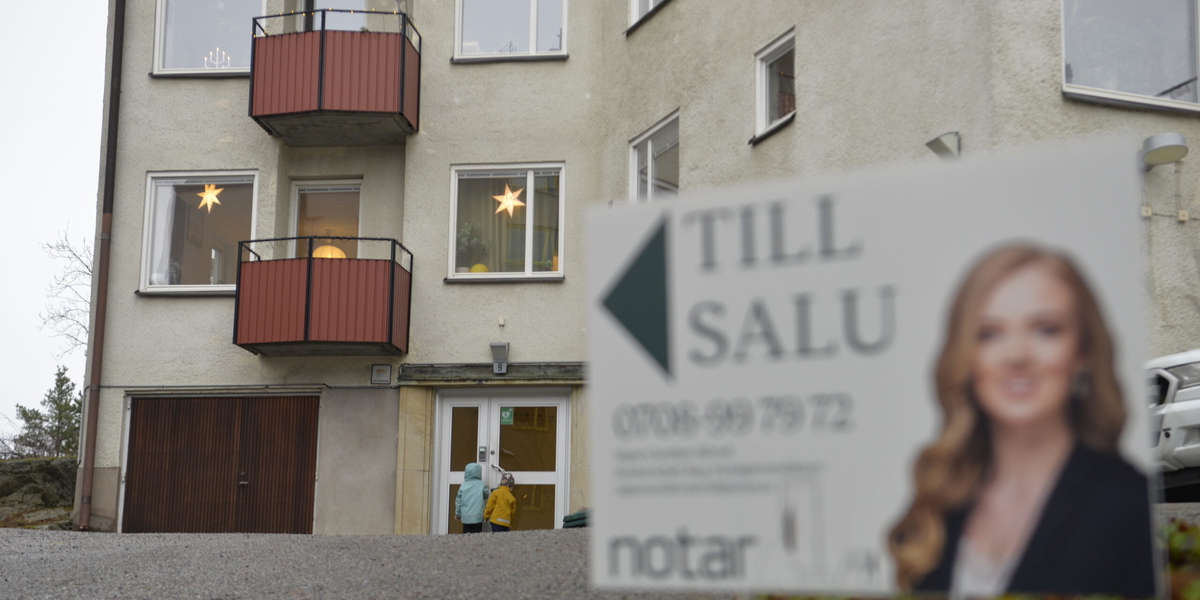 Mäklarskylt framför bostadshus. Två barn framför porten. Arkivbild. 