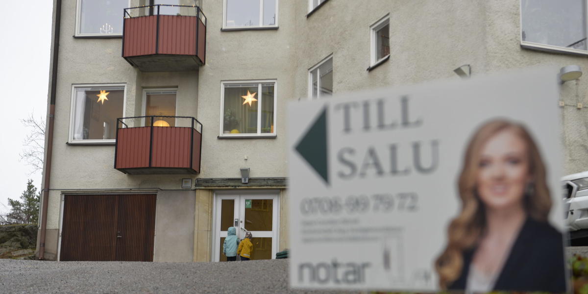 Mäklarskylt framför bostadshus. Två barn framför porten. Arkivbild. 