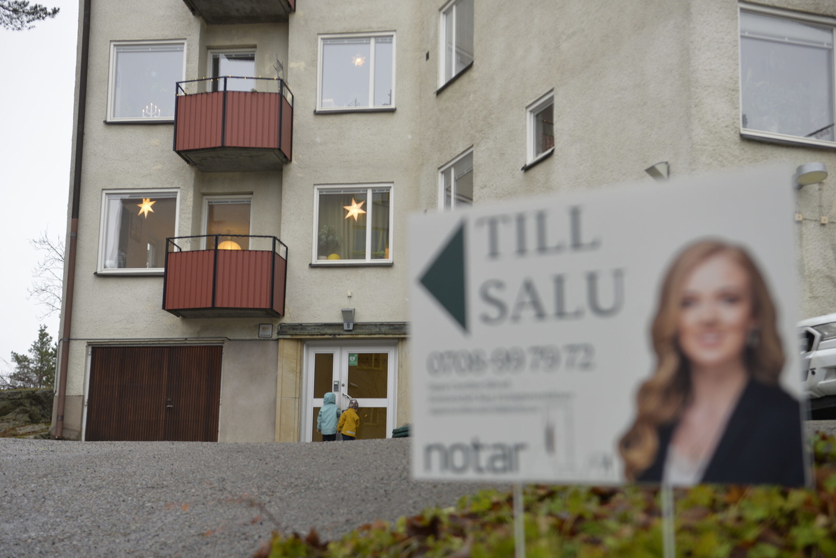 Mäklarskylt framför bostadshus. Två barn framför porten. Arkivbild. 