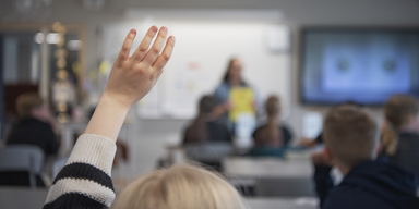 Elev räcker upp handen i klassrum. På en skola i Hässelby jobbar tre pensionärer som volontärer. "Det här är en helt fantastisk skola. Alla tar av sig skorna, räcker upp handen, står bakom bänkarna och lämnar in sin mobil på morgonen", säger en av volontärerna.