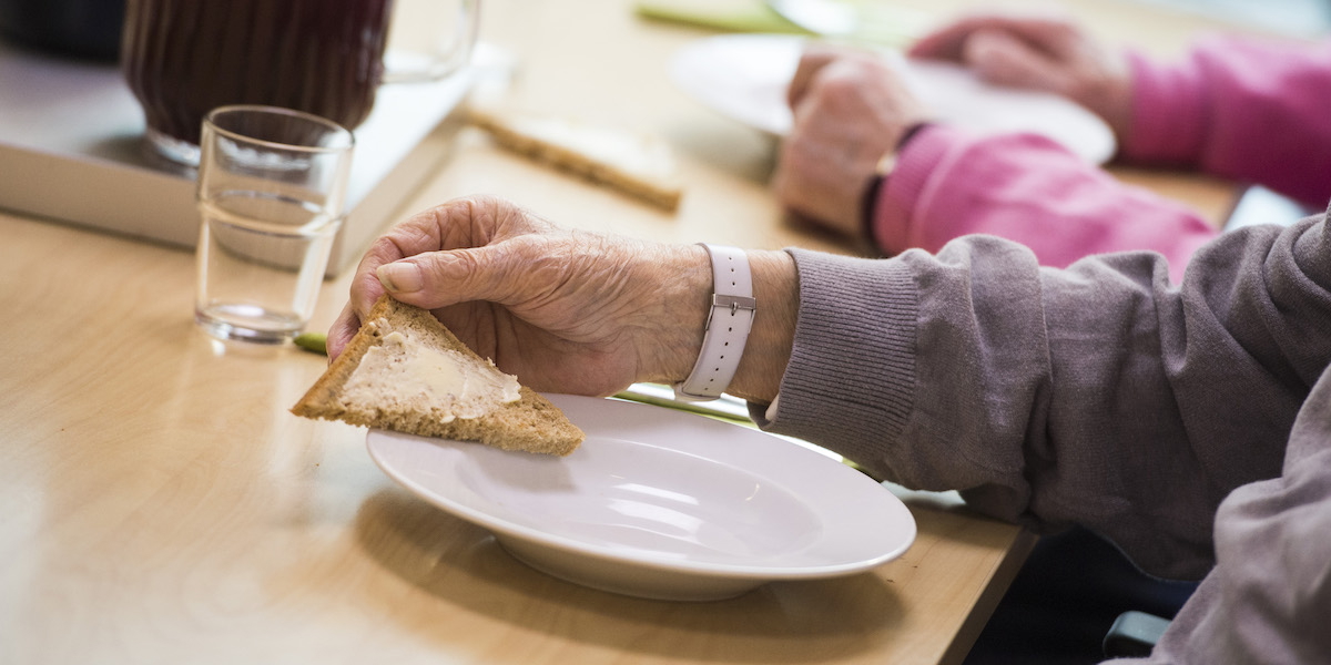 En man på ett äldreboende håller i en liten smörgås med smör. Flera kommuner sparar in på sådant som smör till mackan, nötkött, lax och smaksatt yoghurt inom äldreomsorgen, det visar en undersökning.