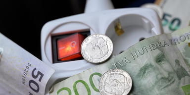 En förgreningsdosa med röd av och på knapp på vägg och pengar. Här får du tips på hur du kan spara pengar genom att minska din elförbrukning