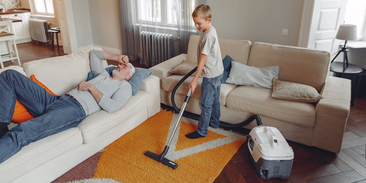 En liten pojke dammsuger medan en man ligger i soffan. Är det okej att betala barn för att de ska hjälpa till med vardagssysslor i hemmet? Ganska många föräldrar med minderåriga barn tycker det.