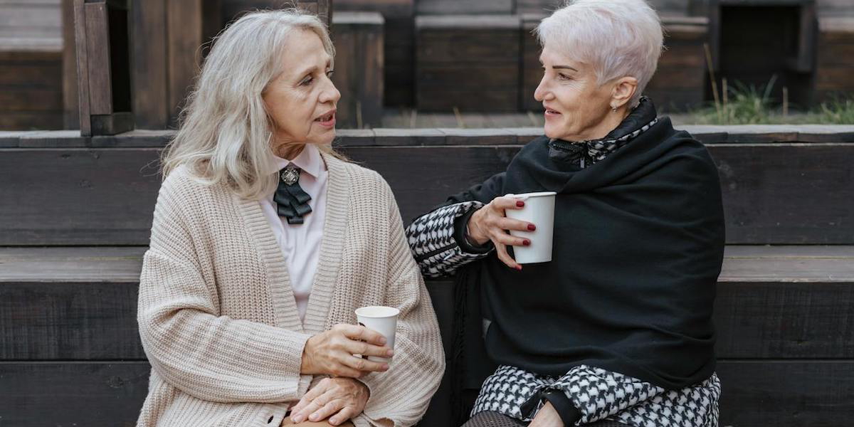 Två kvinnor fikar och pratar. Två pensionärer, dock inte kvinnorna på bilden, tipsar om hur ditt liv som pensionär ska bli bra och ett av deras tips är att du ska vårda dina sociala relationer.