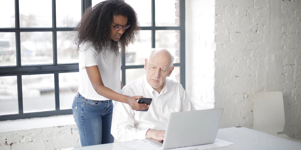 En ung kvinna hjälper en äldre man med mobil och dator. Seniortorget i Umeå har nominerats till en av Europas mest uppmärksammade utmärkelser för samhälls- och politiknära innovation, ett av intitiativen är ett samarbete där studenter hjälper seniorer med digital kunskap och minskar äldres digitala utanförskap.