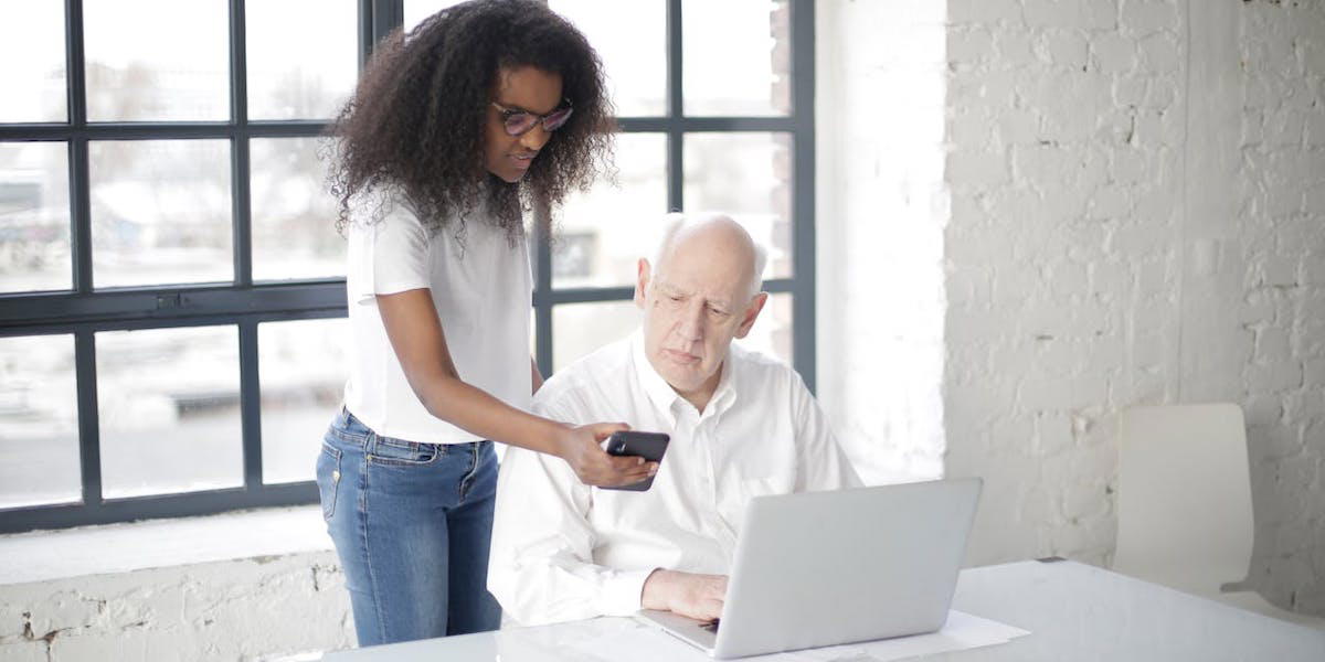 En ung kvinna hjälper en äldre man med mobil och dator. Seniortorget i Umeå har nominerats till en av Europas mest uppmärksammade utmärkelser för samhälls- och politiknära innovation, ett av intitiativen är ett samarbete där studenter hjälper seniorer med digital kunskap och minskar äldres digitala utanförskap.