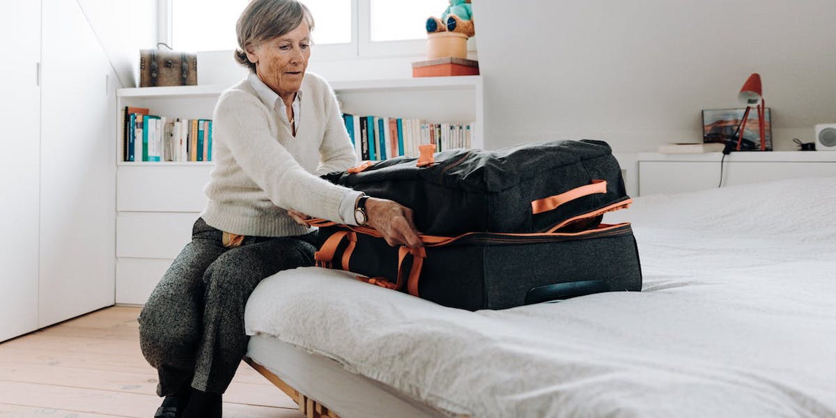 En kvinna stänger en stor resväska. För att slippa släpa runt på en väska du knappt kan bära är det bra att inte packa mer än du behöver och bara de kläder du faktiskt kommer ha på dig, det är ett bra resetips för pensionärer.