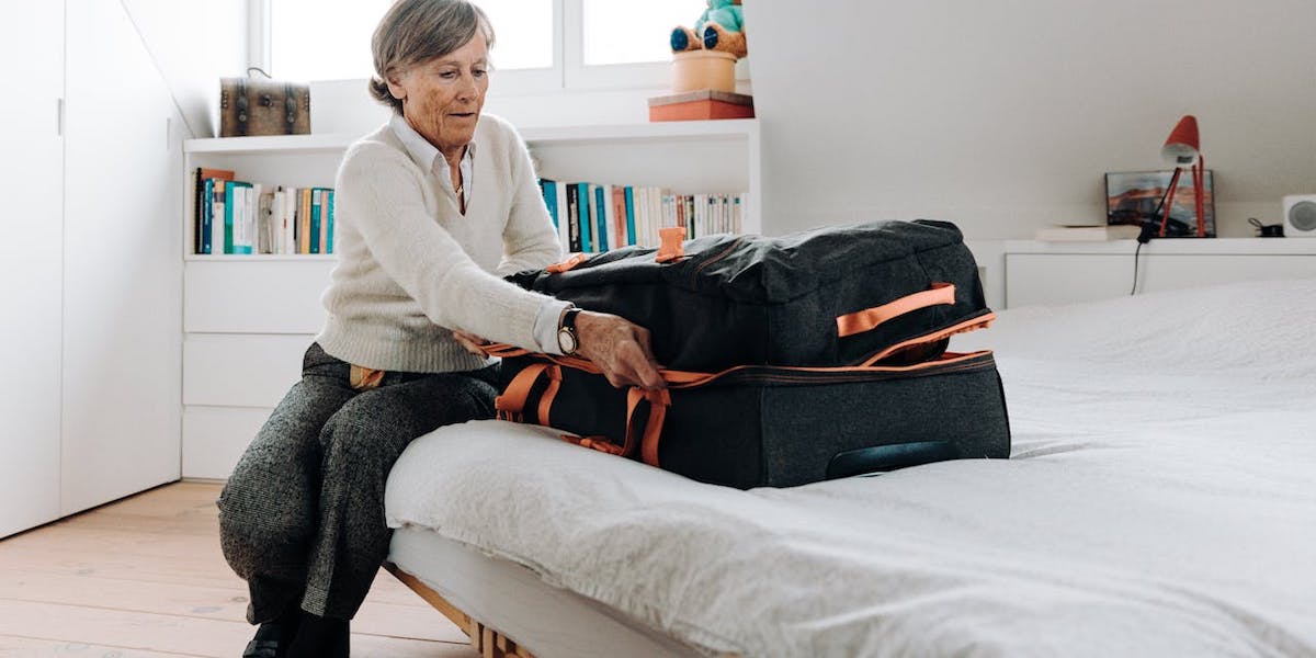 En kvinna stänger en stor resväska. För att slippa släpa runt på en väska du knappt kan bära är det bra att inte packa mer än du behöver och bara de kläder du faktiskt kommer ha på dig, det är ett bra resetips för pensionärer.