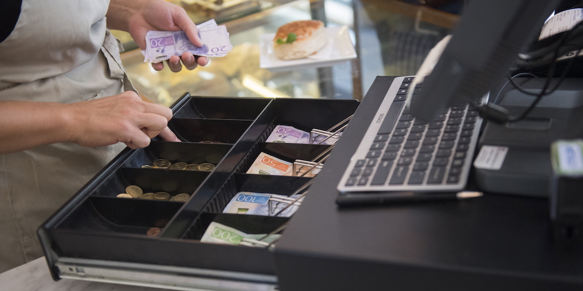 Personal hanterar kontanter i kassa i butik.