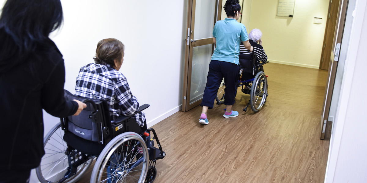 Personal drar två boende på ett äldreboende i rullstol. Två vård-forskare skriver i en debattartikel att det inte tycker att det är fel med språkkrav i äldrevården men att regeringens förslag i propositionen om det är halvfärdigt.