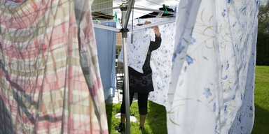 En kvinna hänger tvätt utomhus på en torkvinda. Enligt en textilforskare är det inte alltid nödvändigt att tvätta sängkläderna efter att en göäst har sovit i dem, men när du tvättar är det bästa att, när det går, låta dem lufttorka i solen.