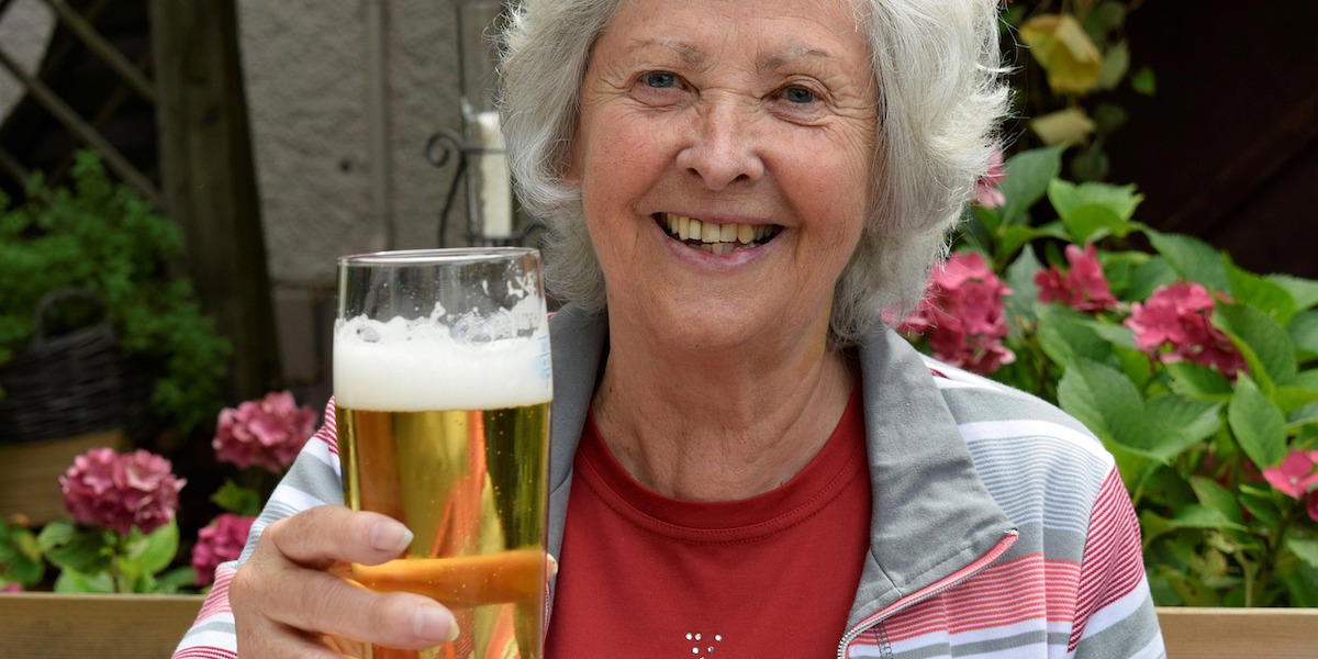 En glad äldre kvinna skålar med en öl. En studie visar att äldre svenskar är lyckligare än unga svenskar, de äldre har starka nära relationer och känner mindre ensamhet än sina yngre släktingar.