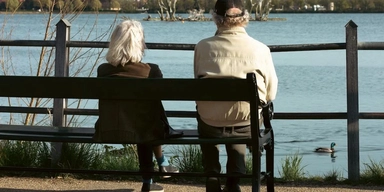 Ett äldre par sitter på en bänk och tittar på en sjö. En spansk studie lyfter fram det svenska pensionssystemet som om en modell för ekonomisk hållbarhet och effektivitet.