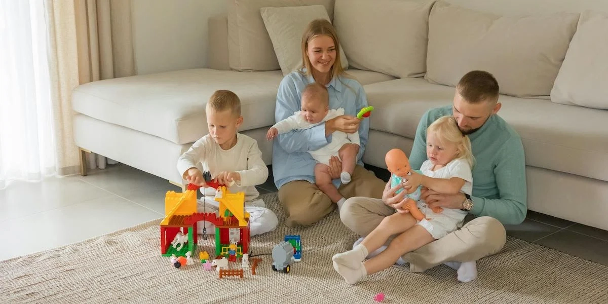 En mamma, en pappa och tre små barn sitter på golvet. En ny undersökning visar att fler svenska föräldrar än föräldrar i övriga nordiska länder tycker att belastningen av att få ihop vardagen påverkar familjens välmående negativt.