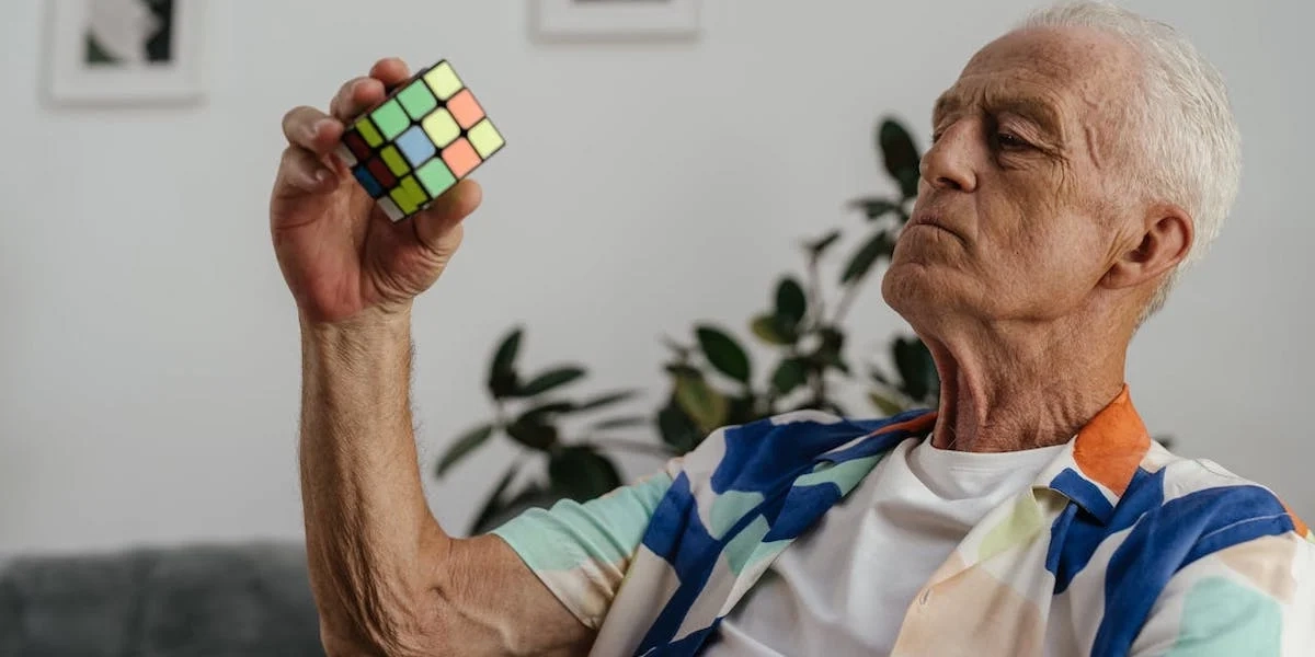 En man tittar på en Rubriks kub. Det finns några saker du kan göra för att hjälpa din hjärna att vara hälsosam längre, exempelvis fortsätta att lära dig ny saker, kanske vill du lära dig att lösa en Rubriks kub?