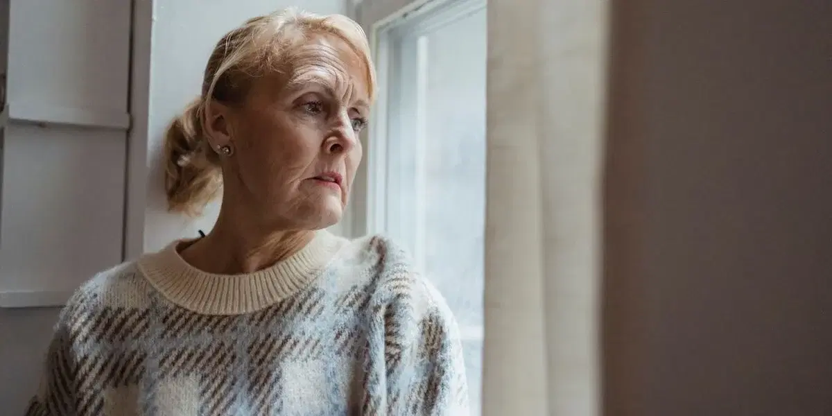 En kvinna tuttar ut genom ett fönster. Pensionärsorganisationer i Linköping vill motverka ensamhet bland äldre och anordnar ett seniorläger för personer från 65 år och uppåt.