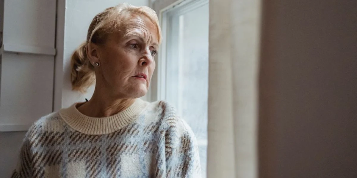 En kvinna tuttar ut genom ett fönster. Pensionärsorganisationer i Linköping vill motverka ensamhet bland äldre och anordnar ett seniorläger för personer från 65 år och uppåt.