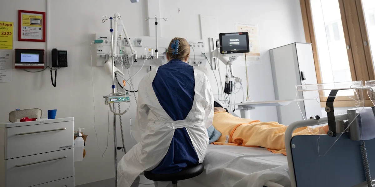 en sjuksköterska vid en patients sjuksäng på ett sjukhus. Sverige har byggt ett system som är bra på att behandla sjukdom, men sämre på att hjälpa människor att förbli friska.