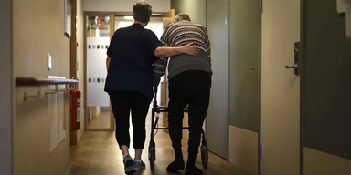 En person går med rullator med ett vårdbiträde bredvid på ett omsorgsboende för äldre. En analys av en undersökning från Socialstyrelsen visar att de flesta äldre är nöjda med sin äldreomsorg.
