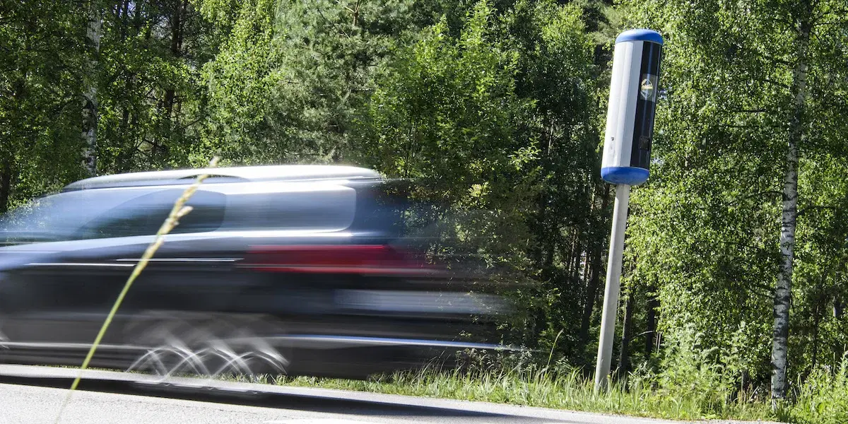 En bil kör förbi en fartkamera. Det finns en dold gräns för när fartkameran slår till och tar en bild.