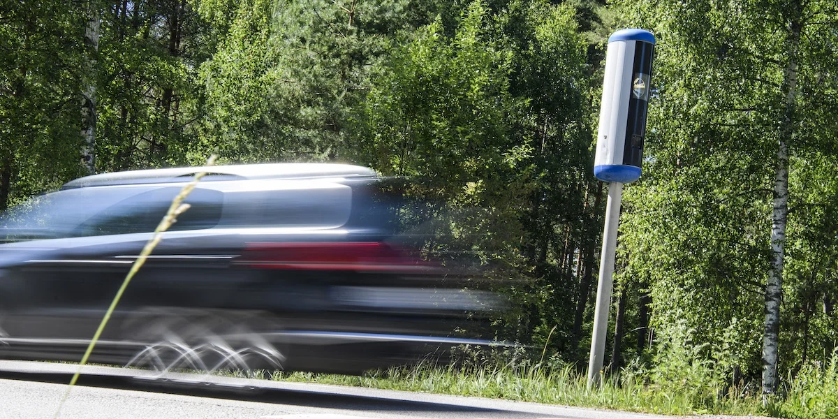 En bil kör förbi en fartkamera. Det finns en dold gräns för när fartkameran slår till och tar en bild.