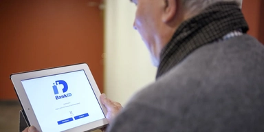 En man håller i en surfplatta med bank-id. Ett bedrägeri börjar ofta med att en okänd person tar kontakt och slutar med en banköverföring, och skyddet för den som har blivit lurad av en bedragare att använda sitt bank-id har varit svagt.