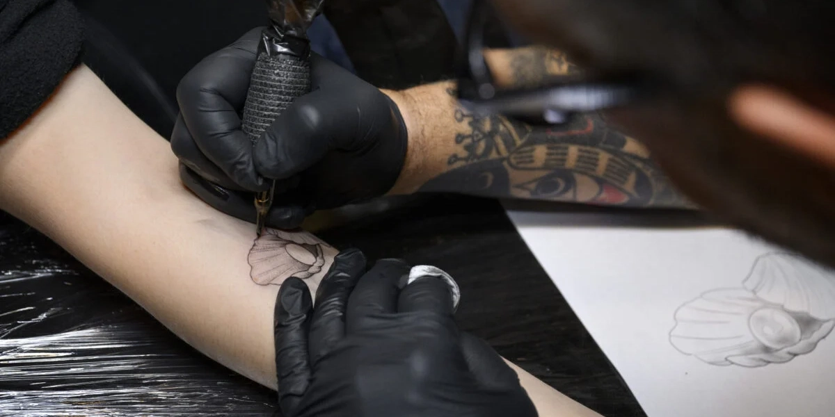 En tatuerare tatuerar in en pärla på en arm. Arkivbild. 