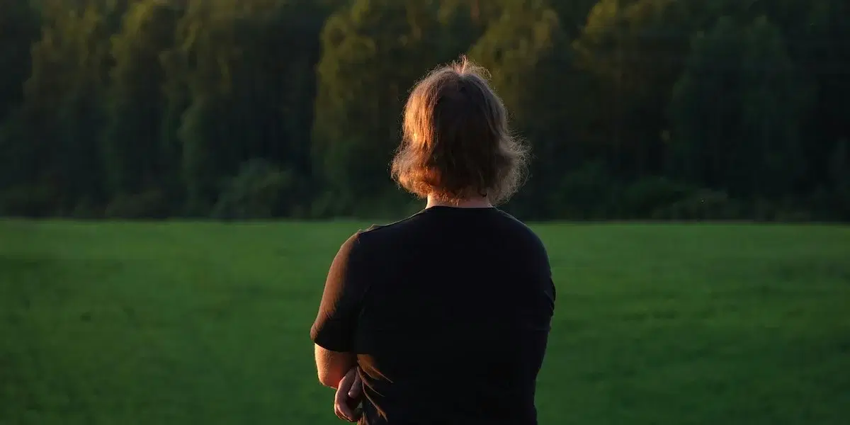 En kvinna tittar mot skogsbrynet. Sorgen tar inte semester, 600 000 svenskar upplever den starkare under ledigheten.