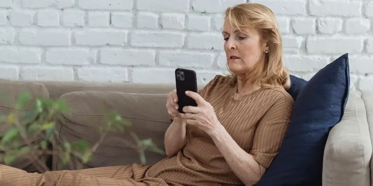 En kvinna sitter i soffa och kollar på sin mobil. Forskare har funnit ett samband mellan hur lång tid människor är stillasittande vid varje enskilt tillfälle och risken att dö i cancer.