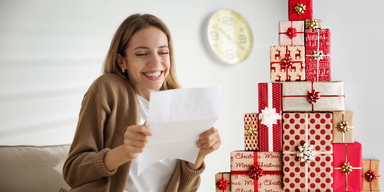 En kvinna är glad över ett prev och en stapel med julklappar. SPP har ett ovanligt förslag till årets julklapp i år och föreslår att arbetsgivare ska stoppa tjänstepensionen i paketet i stället för andra julgåvor till sina anställda.