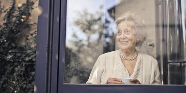en kvinna tittar ut genom ett stort fönster. Hon har byggt upp ett ekonomiskt skyddsnät genom att sparat småsummor i nästan 40 år och det gör bland annat att hon kan bo kvar i sitt stora fina hus. Kvinnan på bilden har ingenting med texten att göra.