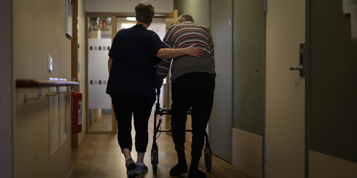 En person går med rullator med ett vårdbiträde bredvid på ett omsorgsboende för äldre. När en kommun inte kan erbjuda plats på särskilt boende inom en skälig tid kan den få betala en straffavgift.